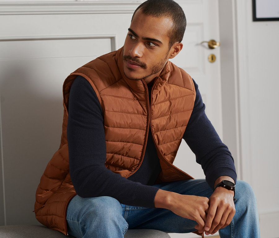 Un homme est assis et porte un gilet matelassé couleur cognac.
