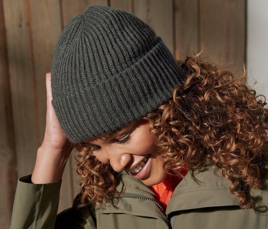 Femme souriant et touchant un bonnet en maille vert.