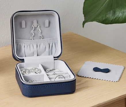 Une petite boîte à bijoux ouverte avec des bijoux à l'intérieur est posée sur une table à côté d'une lampe.