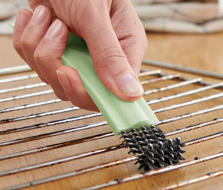 Un homme nettoie une grille de four avec une brosse à four avec racloir.