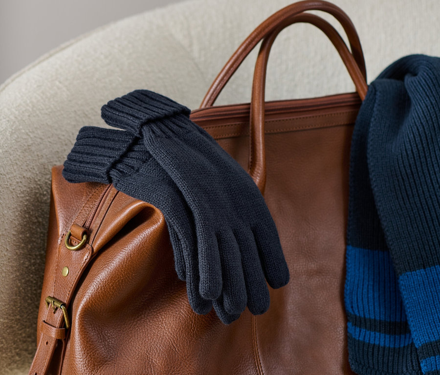 Des gants en maille sont posés sur un sac en cuir marron avec une écharpe en maille.