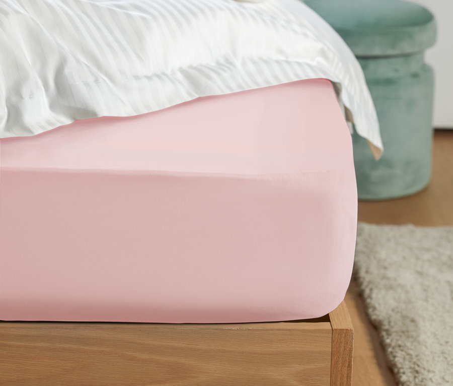 Gros plan d'un drap-housse rose sur un lit avec du linge de lit rayé blanc et un tabouret vert à l'arrière-plan.