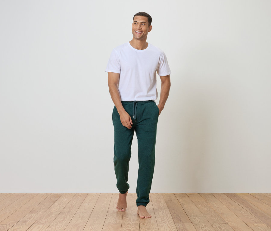 Homme marchant pieds nus en pantalon de survêtement vert et t-shirt blanc.