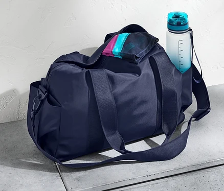 Un sac de sport bleu marine et une bouteille d'eau sur une surface en béton.