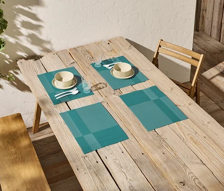 Table à manger en bois avec quatre sets de table turquoise, chacun contenant un bol, une assiette, des couverts et un verre.