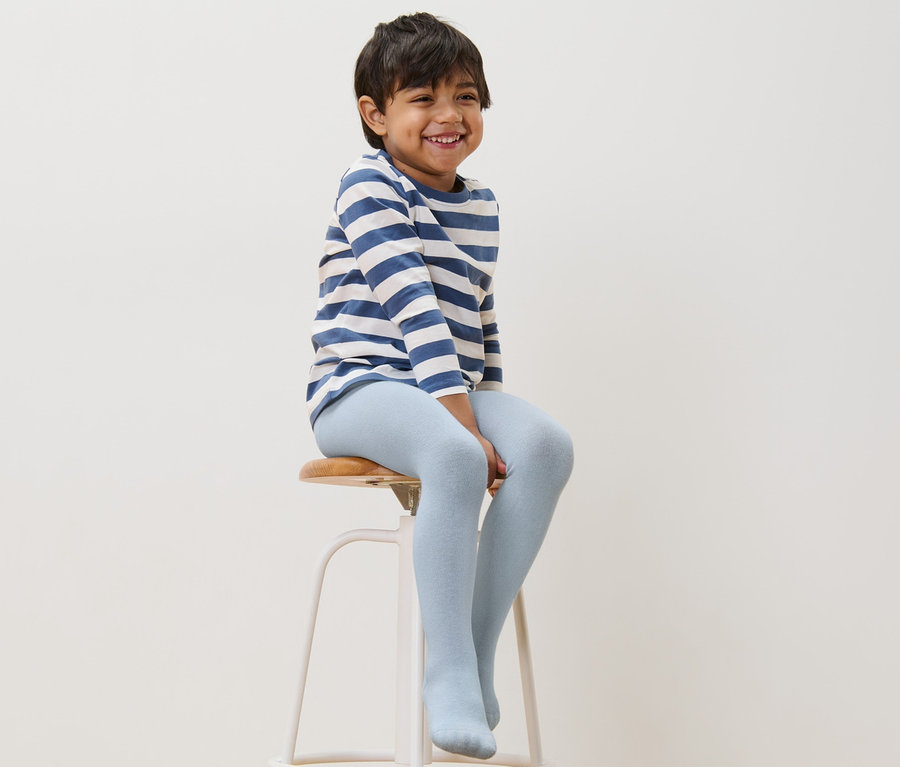 Un garçon est assis sur un tabouret et porte des collants en coton bleus.