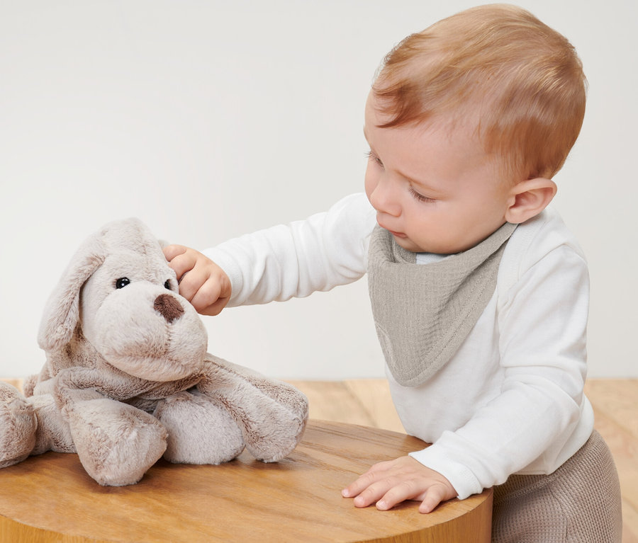 Bébé touchant un chien en peluche et portant 2 foulards en mousseline pour bébé.
