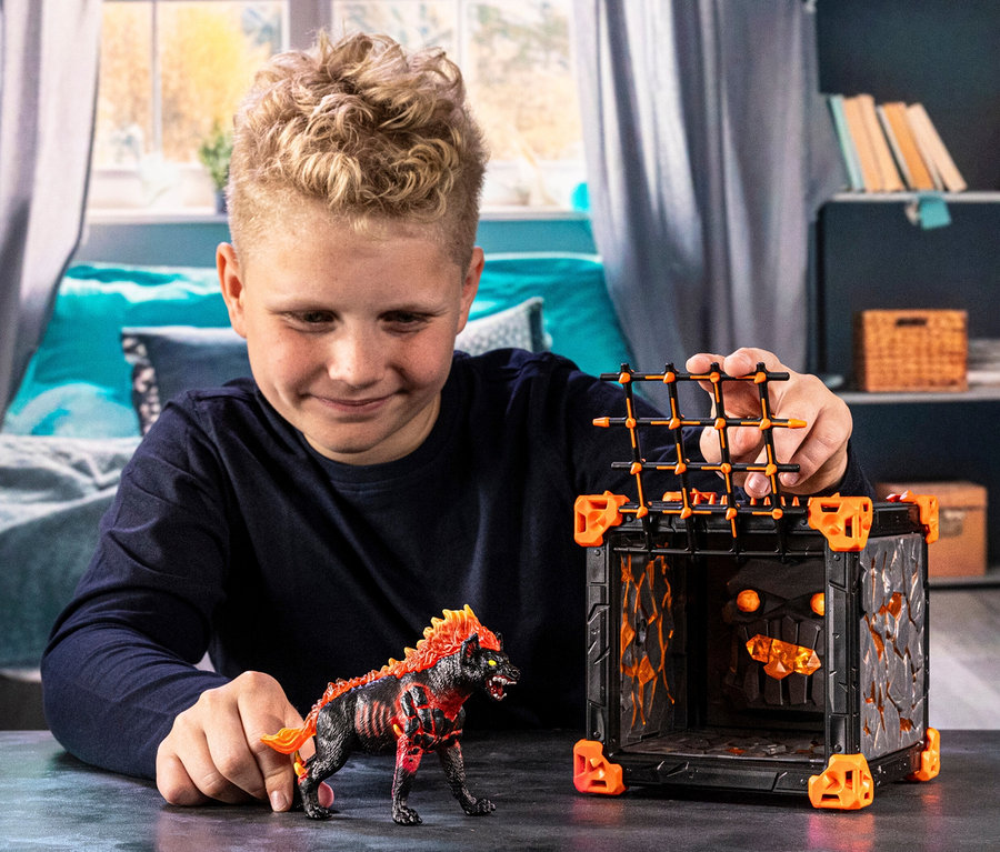Un garçon joue avec la hyène de lave BattleCave Eldrador de Schleich et le BattleCave Eldrador de Schleich.