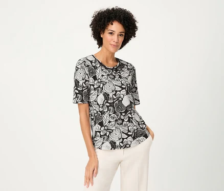 Une femme aux cheveux bouclés porte un T-shirt Olsen à motifs floraux et un pantalon clair.