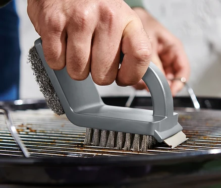 Homme nettoyant une grille de barbecue avec une brosse de nettoyage 3 en 1.