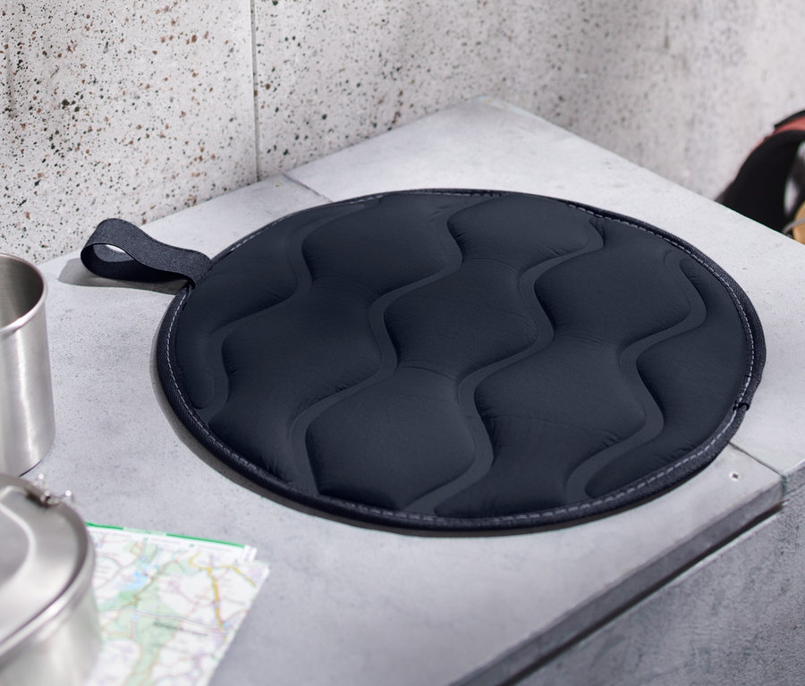 Un coussin d’assise thermique pliable est posé sur un banc en béton gris.