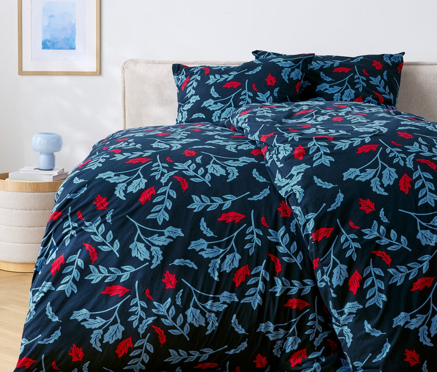 Lit avec des draps bleu foncé avec des feuilles rouges et bleues.