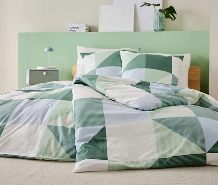 Un lit avec une courtepointe patchwork verte, blanche et bleue et des taies d'oreiller assorties dans une chambre.
