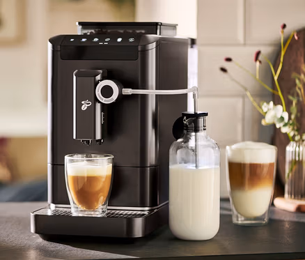 Une machine à café entièrement automatique « Esperto 2 Milk » Granite Black prépare du café dans un verre. À côté se trouve une carafe à lait.