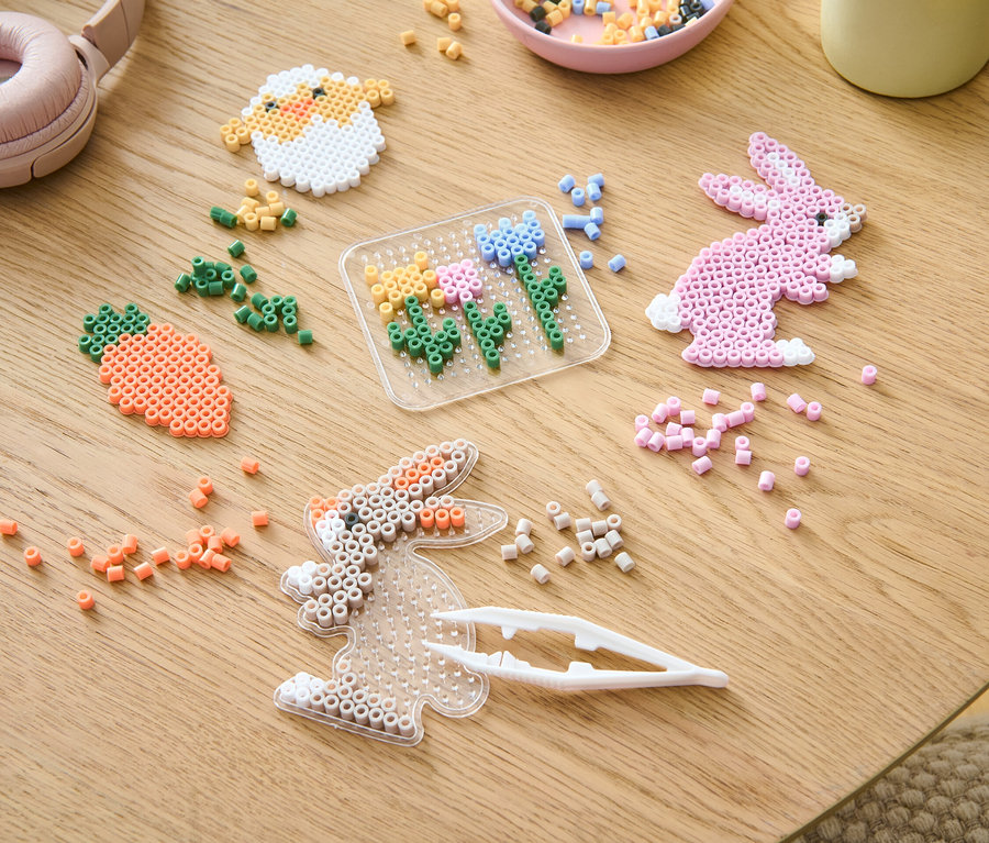 Sur une table se trouvent un set de bricolage Perles à repasser et des perles de différentes couleurs.