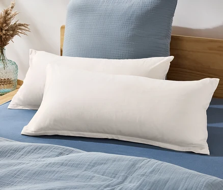 Deux taies d'oreiller en jersey sont posées sur un lit avec un drap et une couverture bleus.