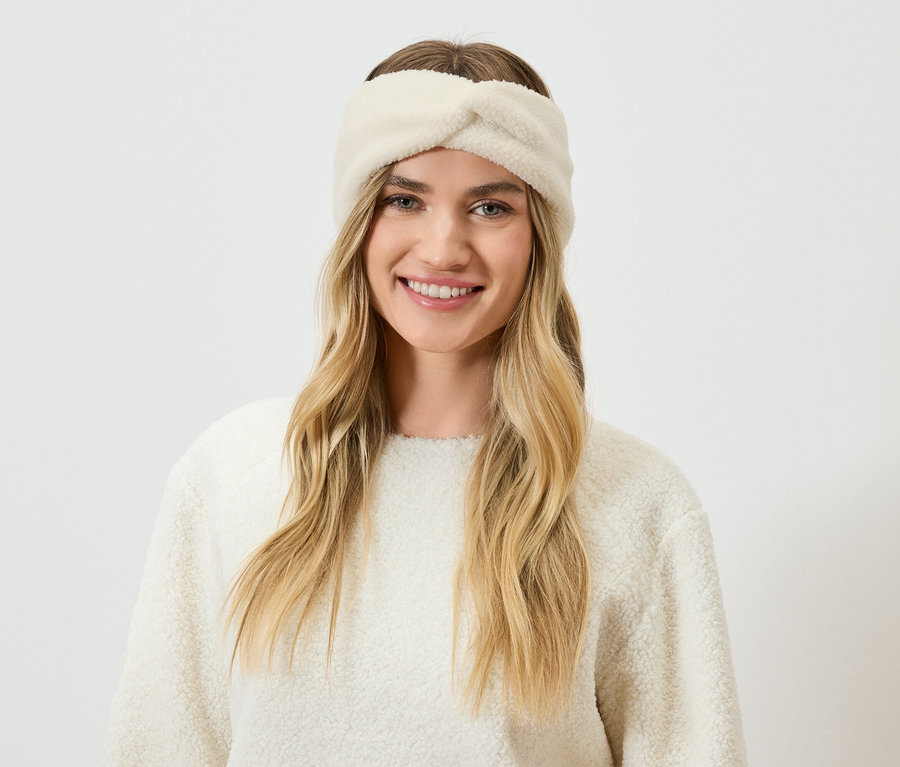 Portrait d'une femme souriante aux cheveux blonds portant un bandeau et un pull crème.