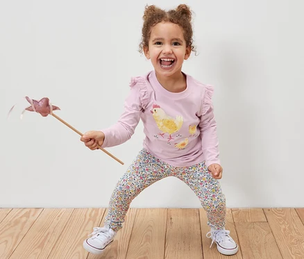 Fillette souriante tenant une baguette magique et portant un 2 Leggings pour enfant, rose et un t-shirt imprimé poulet.