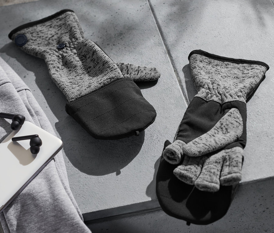 Deux moufles convertibles en maille polaire sont posées sur une table en béton grise à côté d'un sweat-shirt gris, d'un téléphone blanc et d'écouteurs noirs.