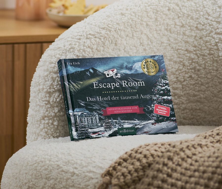 Sur un fauteuil se trouvent un livre calendrier de l’Avent Escape Room « Das Hotel der tausend Augen » (L’hôtel aux milles yeux, en allemand) et une couverture beige.