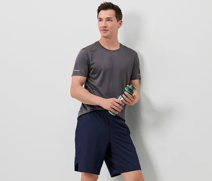 Un homme portant un t-shirt gris tient une bouteille d'eau verte et porte un short de sport.