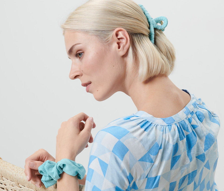 Une femme blonde est assise dans un fauteuil, portant un élastique à cheveux au poignet et une pince à cheveux. Ensemble d'accessoires à cheveux.