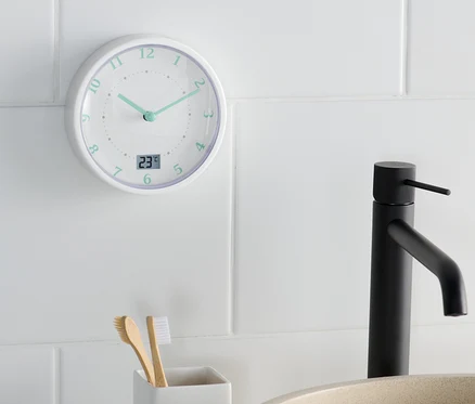 Une horloge murale de salle de bain indique 11h22 à côté d'un lavabo et d'un porte-brosses à dents.