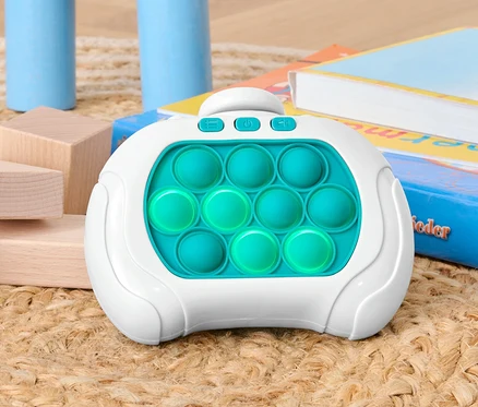 Un jeu Pop-It est posé sur un tapis entre des blocs de bois et des livres.