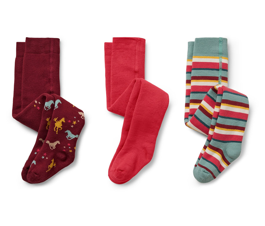 Sur un fond blanc, trois collants pour enfants : bordeaux avec des chevaux et des étoiles, rouge et rayé avec du turquoise, du rouge, du jaune et du blanc.