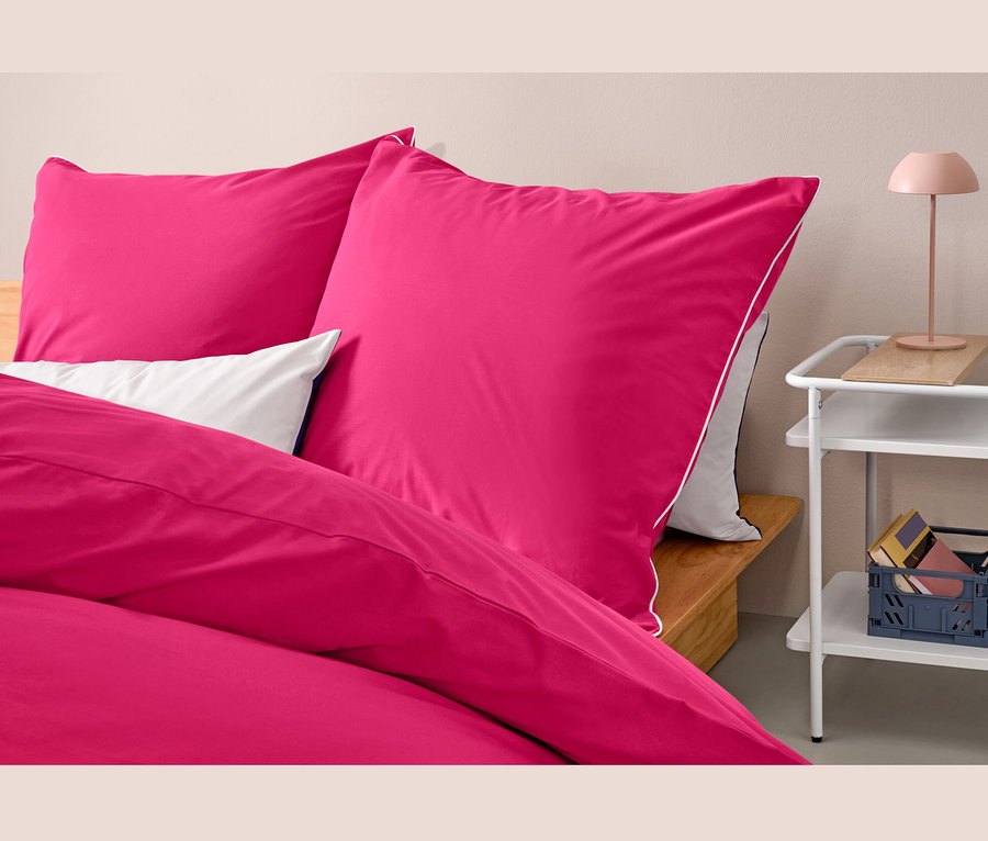 Gros plan de trois ensembles de parure de lit rose en renforcé de taille standard sur un lit à côté d'une table.