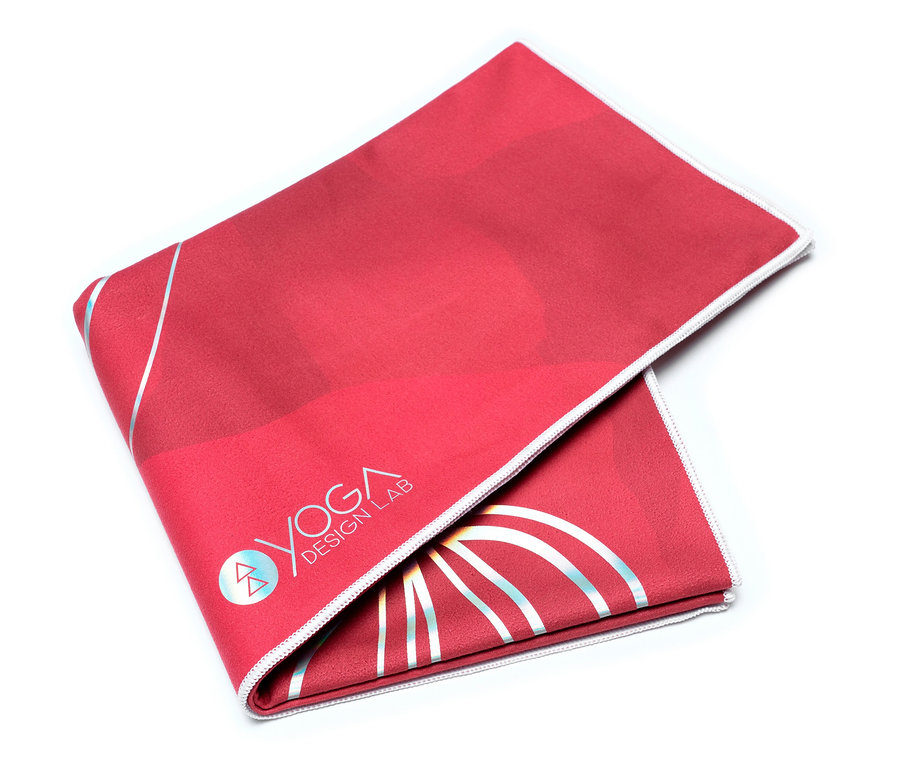Une serviette de yoga rouge avec le logo Yoga Design Lab, pliée sur un fond blanc.