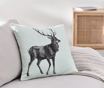 Une housse de coussin décoratif avec un motif de cerf est posée sur un canapé.
