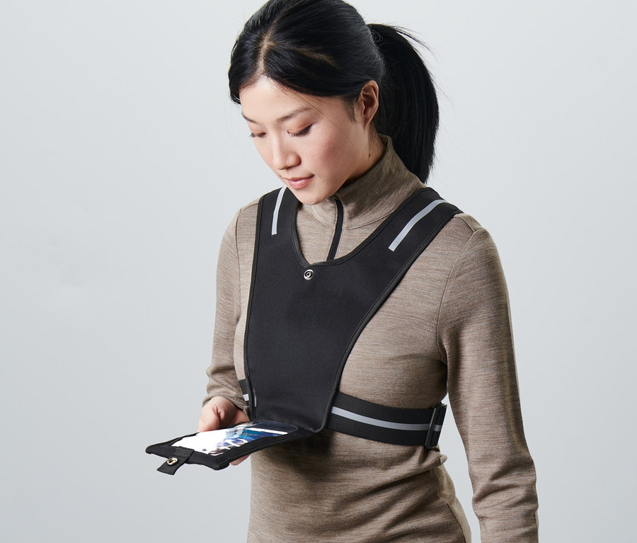 Une femme tient un smartphone dans la poche d'un gilet de course noir.