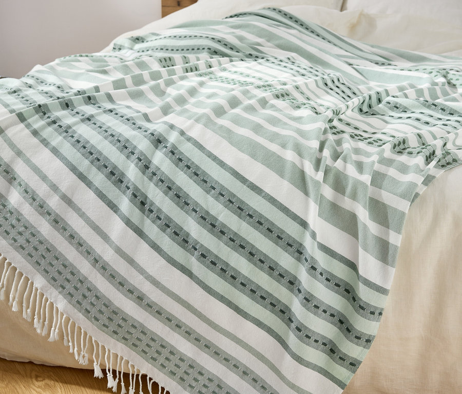 Un plaid rayé vert et blanc avec des franges est posé sur un lit.