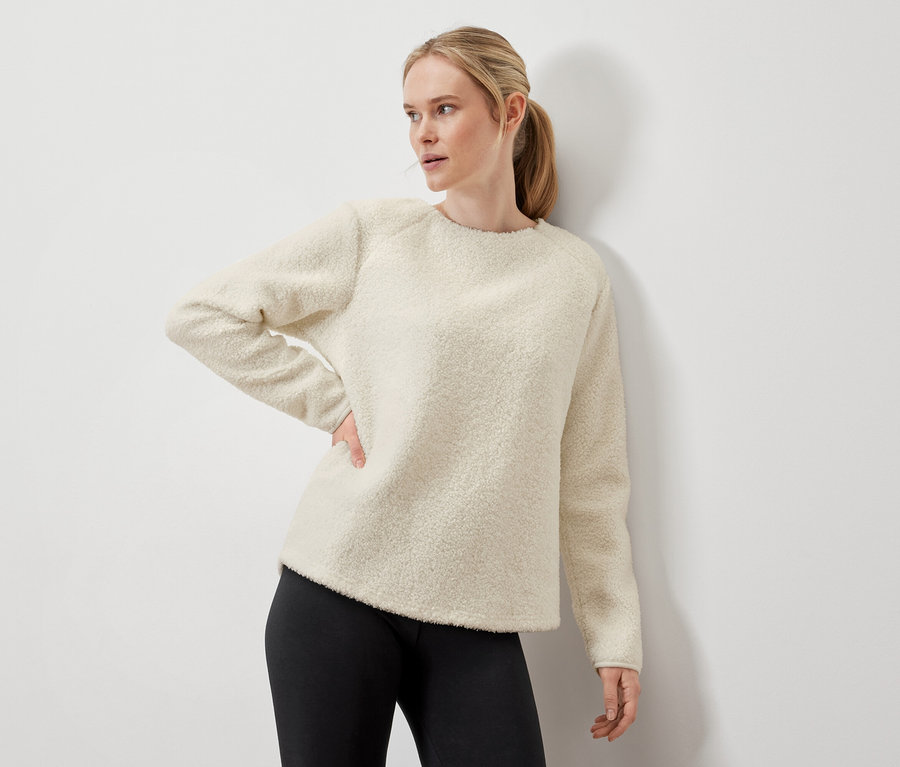 Femme posant dans un pull crème et un legging noir.