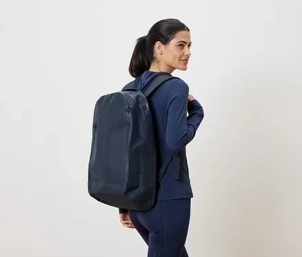 Une femme en survêtement bleu marine avec un sac à dos bleu marine sur l'épaule regarde par-dessus son épaule.