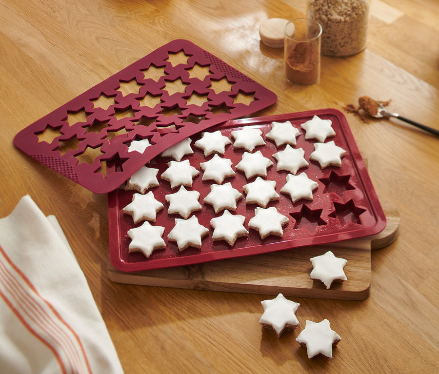 Sur une table en bois, un tapis de cuisson rouge pour étoiles à la cannelle avec des étoiles cuites.