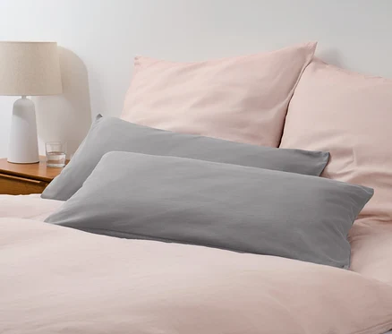 Deux taies d'oreiller en jersey gris sur un lit avec du linge de lit rose.