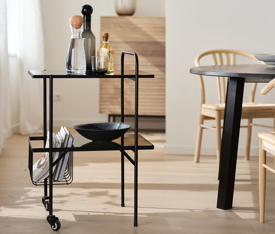 Desserte de cuisine noire avec étagères en verre et roulettes, avec boissons et saladier.