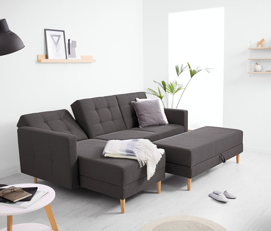 Un canapé-lit d’angle avec cœur à ressorts et banquette de rangement est dans le salon. Il y a une lampe et une étagère en arrière-plan.