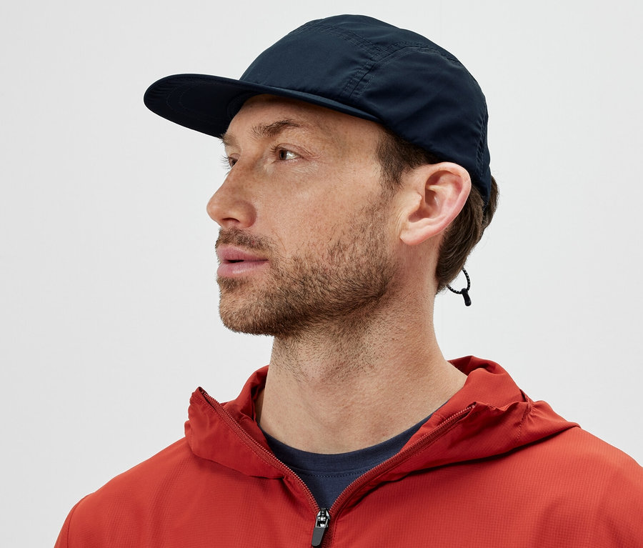 Un homme portant une veste orange et une casquette pliable regarde vers la gauche.