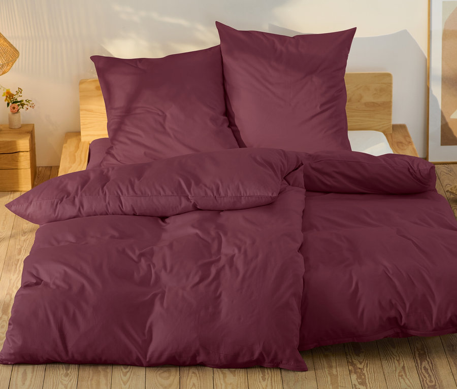 Linge de lit bordeaux sur un lit avec un cadre en bois.