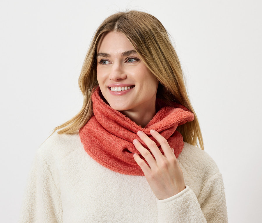 Une femme aux cheveux blonds porte un snood corail et un pull crème.