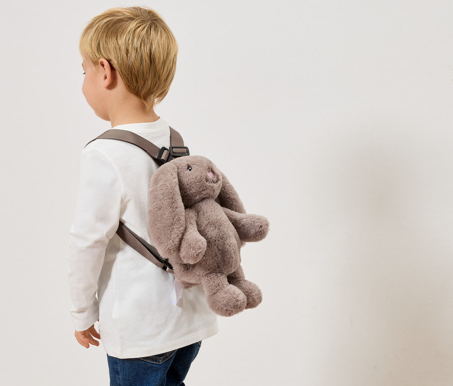 Un enfant porte un sac à dos lapin gris.