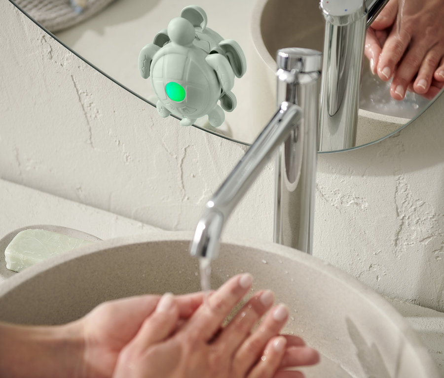 Une personne se lave les mains dans un lavabo ; un minuteur pour se laver les mains et les dents est fixé à un miroir.
