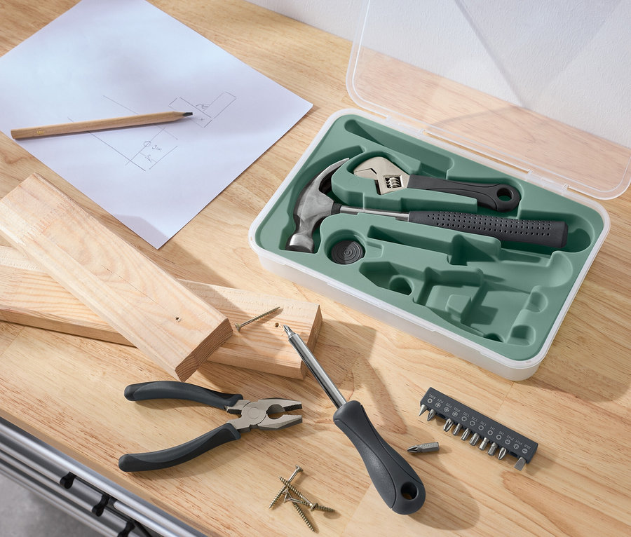 Sur une table sont posés un jeu d'outils, du bois, un tournevis, une pince, des vis, un crayon et un croquis.