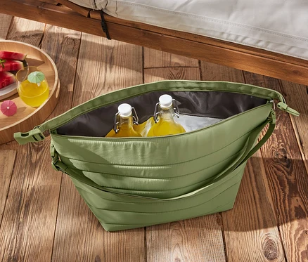 Un sac isotherme vert avec des bouteilles et de la pastèque sur une table en bois.