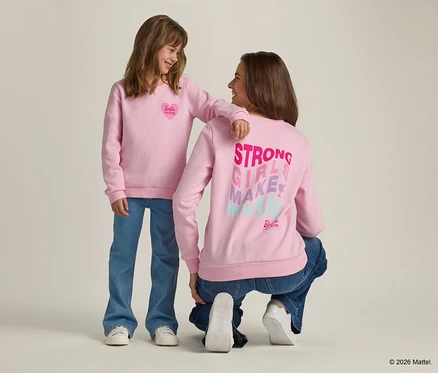 Une fille avec le bras sur l'épaule d'une femme accroupie, toutes deux vêtues de pulls roses et de jeans.