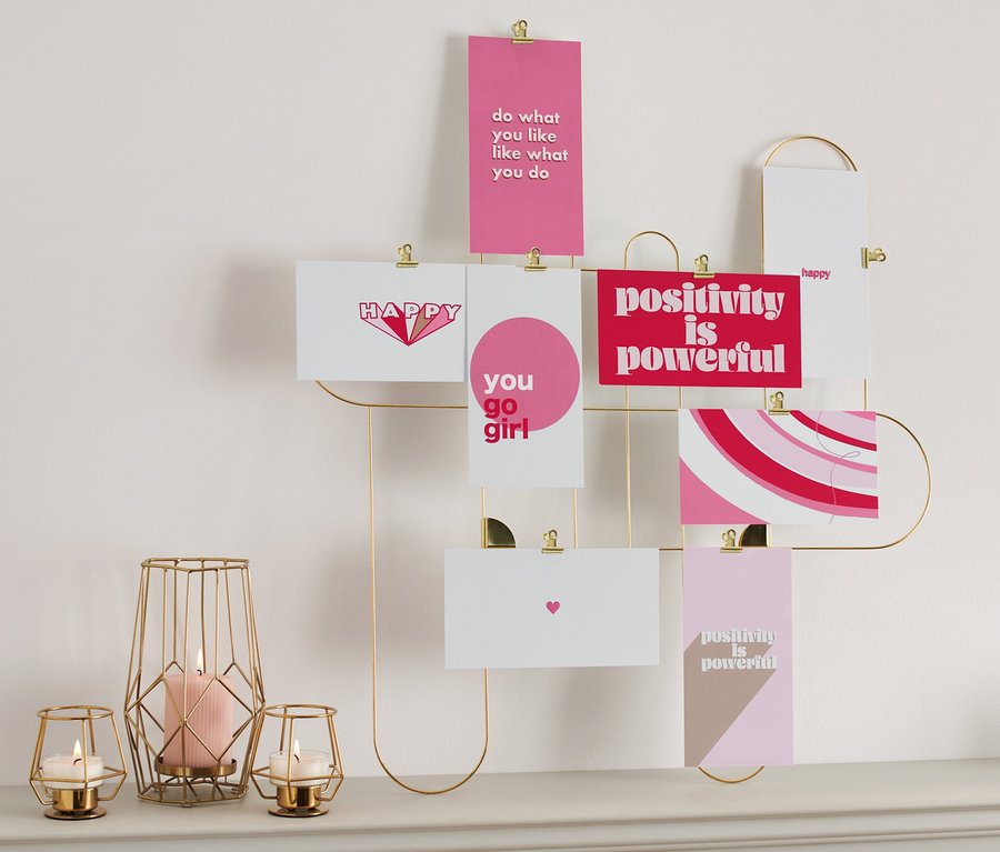 Un lot de cartes postales / mini cartes illustrées est accroché à un cadre doré sur le mur au-dessus d'un dessus de table, sur lequel reposent des bougies et une horloge.