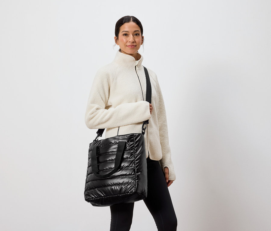 Femme debout avec un sac matelassé noir sur l'épaule.